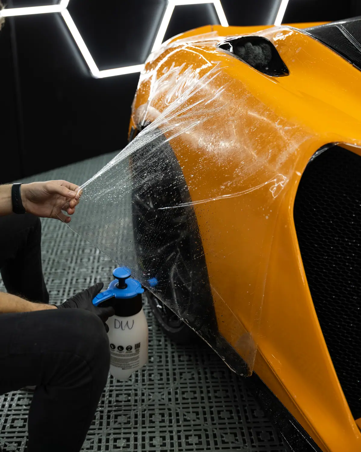 OzoneShield installer laying clear paint protection film on an orange McLaren